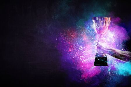 Hand holding up a gold trophy cup against dark backgroundの写真素材