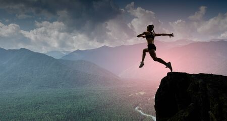 Woman jumping over mountain precipice in front of sunsetの写真素材