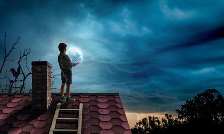 Boy holding moon at night on roof topの写真素材