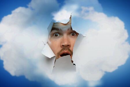 Male face through the hole in paperの写真素材