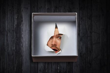 Male face through the hole in paperの写真素材