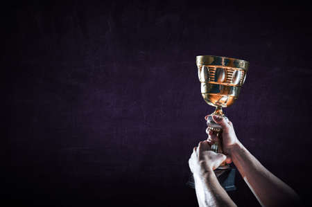 Hand holding up a gold trophy cup against dark background