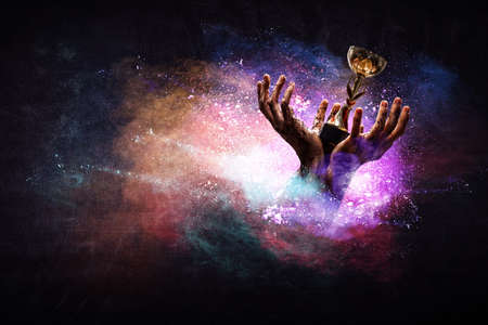 Hand holding up a gold trophy cup against dark backgroundの写真素材