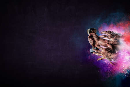 Hand holding up a gold trophy cup against dark backgroundの写真素材