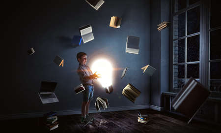 Boy holding a light bulb with books around himの写真素材