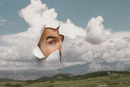 Male face through the hole in paperの写真素材