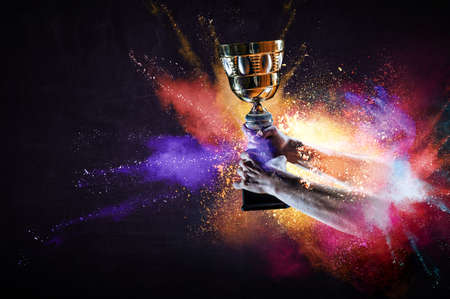 Hand holding up a gold trophy cup against dark backgroundの写真素材