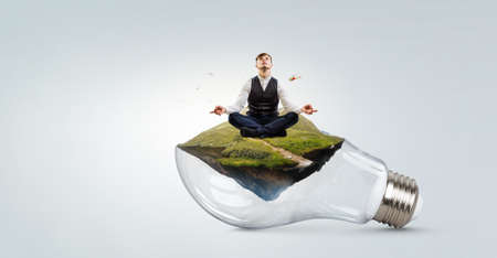 Businessman doing yoga in lotus pose on light bulbの写真素材