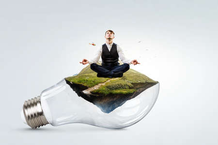 Businessman doing yoga in lotus pose on light bulbの写真素材