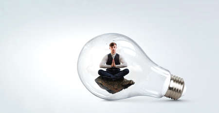 Businessman doing yoga in lotus pose inside light bulb . Mixed mediaの写真素材