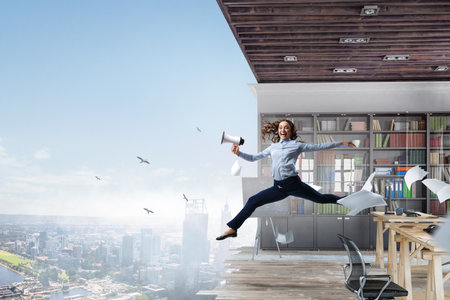 Portrait of energetic businesswoman with megaphone jumping in open airの写真素材
