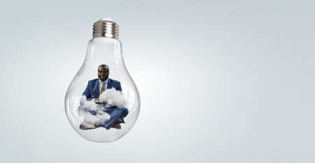 Young black man sitting and meditating inside light bulbの写真素材