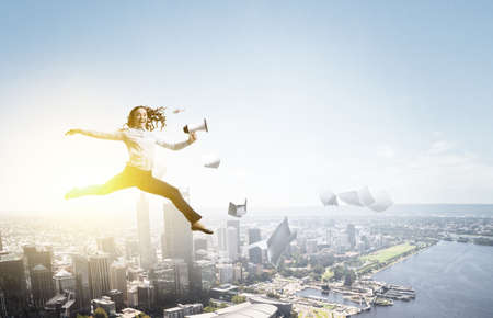 Portrait of energetic businesswoman with megaphone jumping in open air