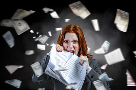 Young stressed woman ripping documents with frustrated facial expression.