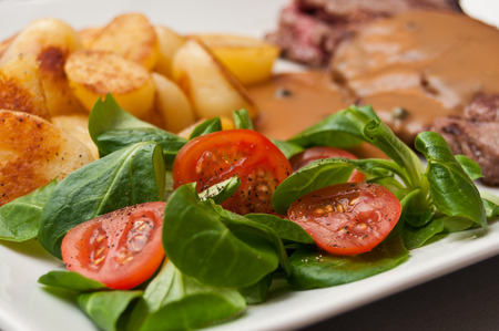 steak grilled with pepper sauce and potatoes and mache cherry tomatoesの写真素材