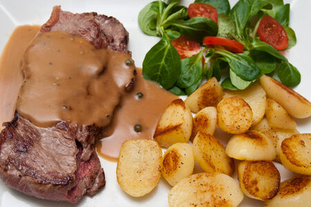 steak grilled with pepper sauce and potatoes and mache cherry tomatoesの写真素材