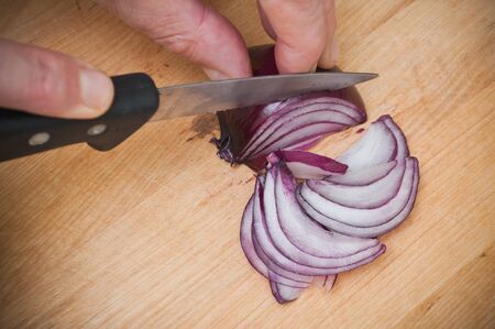 closeup of man cutting a purple onions on wooden cutting board