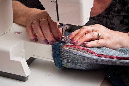 closeup of woman with a sewing machine and blue jeans hem