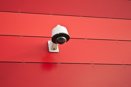 electronic security video camera of surveillance on red modern wall background