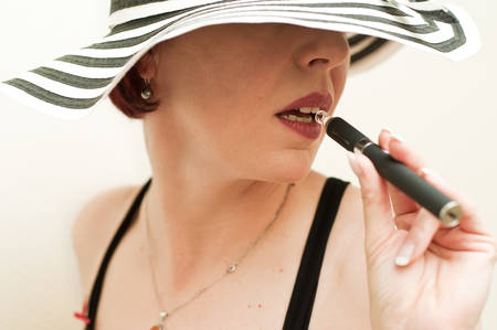 fashion woman with e-cigarette and hat on white backgroundの写真素材