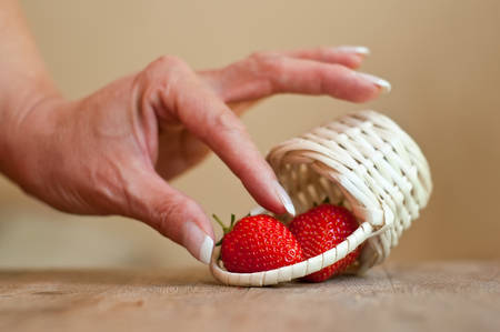 closeup of hand of woman with strawberries in a wooden basket on wooden table backgroundの写真素材