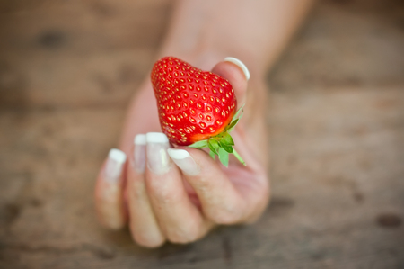 closeup of hand of woman with strawberries  on wooden table backgroundの写真素材