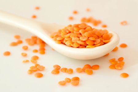 closeup of coral lentils in a spoon on white background