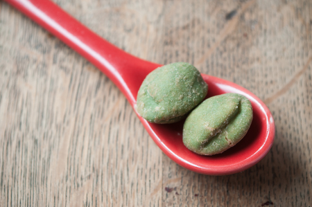 wasabi peas in a  red spoon on wooden backgroundの写真素材