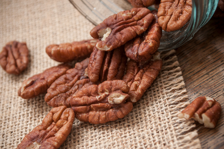 closeup of pecan nuts falling from glass container on wooden table background