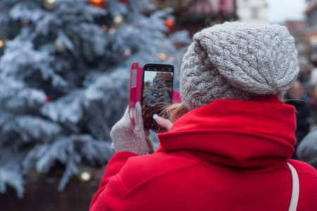 Colmar - France - 14 December 2017 - portrait of tourist with wool hat taking a picture of christmas tree with phone in christmas market のeditorial素材