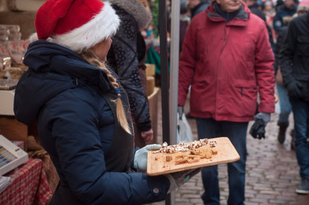 Riquewihr - France - 16 December 2017 - woman with christmas hat tasting gingerbread on wooden cutting board  at the christmas marketのeditorial素材