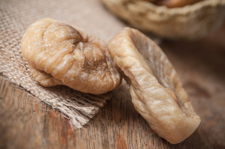 closeup of dried figs falling from basket on wooden background 