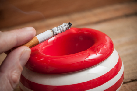 closeup of man with a cigarette on red ashtray on wooden backgroundの写真素材