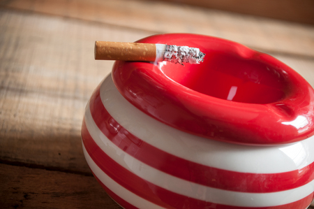 closeup of cigarette on red ashtray on wooden backgroundの写真素材