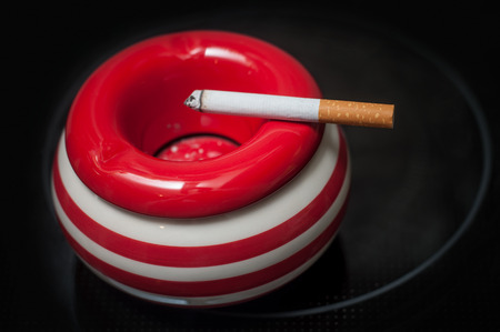 closeup of cigarette on red ashtray on black  background 