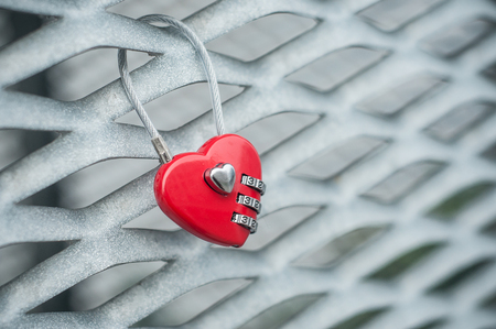 closeup of red padlock in shaped heart on metallic gridの写真素材