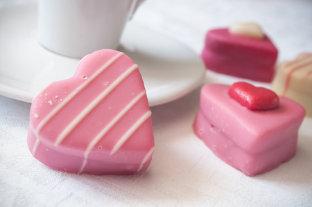 closeup of pink shaped heart pastry and cup of coffe on white napkin for valentines day