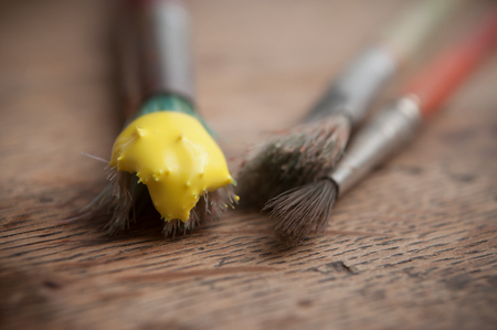 closeup of yellow acrylic paint on brushes on wooden table background の写真素材