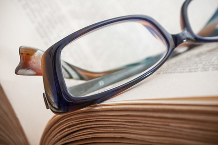 closeup of glasses on ancient book open on wooden table backgroundの写真素材