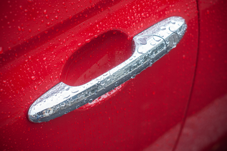 closeup of rain drops on metallic handle on red carの写真素材
