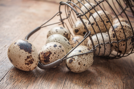 closeup of quail eggs falling from metallic basket on wooden table backgroundの写真素材