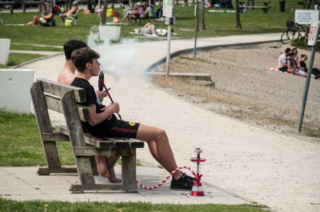 Reiningue - France - 21 May 2018 - two boys smoking shisha on wooden bench in border lake