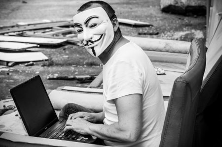 Paris - France - 19 May 2018 - portrait of man with Vendetta mask and coumputer in abandoned  factory  on vintage armchair . This mask is a well-known symbol for the online hacktivist group Anonymousのeditorial素材