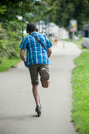 Portrait of man on scooter on the road with headphones on back viewの写真素材
