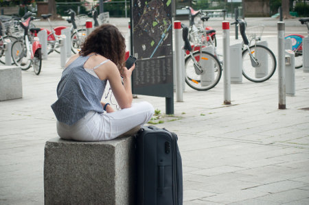 Mulhouse - France - 17 June 2018 - woman with suitcase waiting for the train with smartphone in front of train station on back viewのeditorial素材