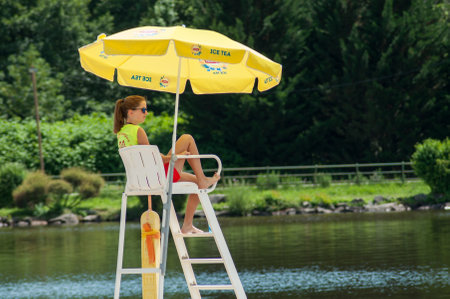 Belfort - France - 19 June 2018 - Lifeguard sitting on chaut with umbrella in front of the lake on back viewのeditorial素材
