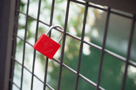 closeup of red padlock with shaped heart on metallic gridの写真素材