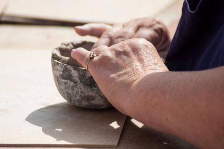 closeup of hands of old woman making clay pottery bowl in outdoorの写真素材