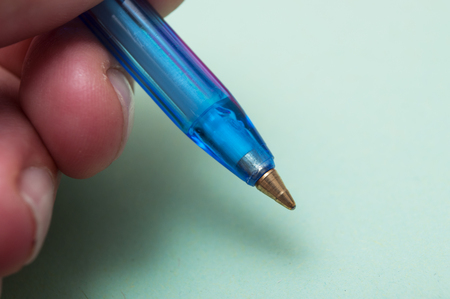 closeup of blue ballpoint pen in hand on green paper background
