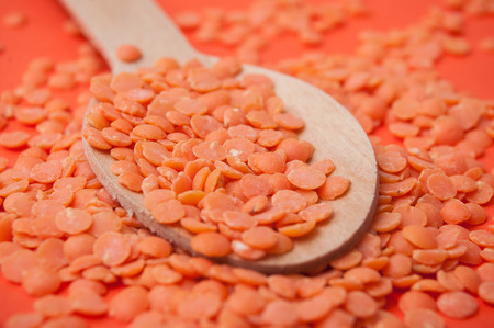 closeup of coral  lentils in a wooden spoon on orange backgroundの写真素材